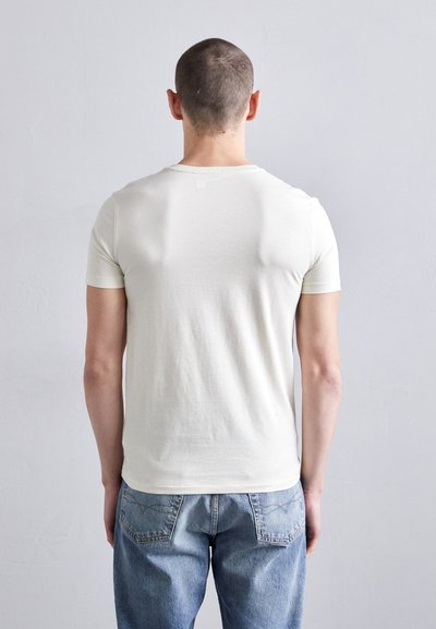 T-shirt à manches courtes couleur blanc cassé en tissu doux, avec un col rond et une texture lisse, associé à un jean en denim bleu clair.