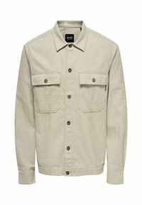 Veste beige à boutons avec manches longues, deux poches poitrine, boutons marron et col, fabriquée en tissu texturé.