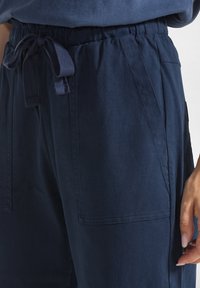 Navy blauwe ontspannen fit broek met een elastische tailleband, trekkoorddetail en zijzakken. Gemaakt van een zachte, gestructureerde stof.