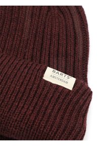 Bordeauxrode gebreide muts met geribbelde structuur, voorzien van een label met de tekst "BARTS AMSTERDAM" in het zwart op een crèmekleurige achtergrond.