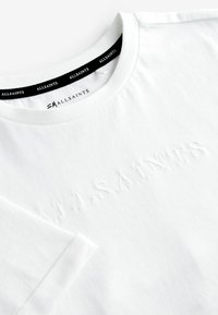 Vit bomulls t-shirt med rund hals och korta ärmar. Har ett präglat logotyp. Mjuk textur, minimalistisk design. Svart etikett vid halslinningen.