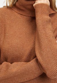 En rostfärgad polotröja gjord av ribbad stickad tyg. Designen har långa ärmar med en avslappnad passform och en mysig, texturerad finish.