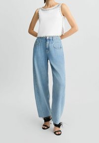 Top bianco senza maniche con bordi di gioielli, abbinato a jeans a gamba larga blu chiaro. Sandali neri con dettagli in piuma completano l'outfit.