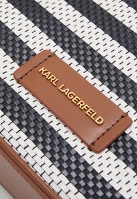 Vävd handväska med svartvita ränder, en brun läderdetalj och en guldfärgad logotypplatta med texten "KARL LAGERFELD".
