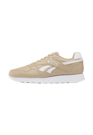 Beige Reebok sneaker met witte zool, witte logostrepen en Reebok-logo aan de zijkant, gezien vanaf de buitenkant.