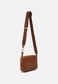 Sac en cuir marron en bandoulière de forme rectangulaire, avec une surface texturée, des accessoires en or et une sangle réglable arborant une marque.