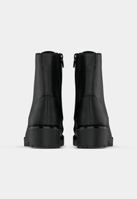 Paire de bottines noires à talons carrés avec fermetures éclair à l'arrière, vues de dos sur un fond blanc uni.