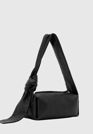 Schwarze rechteckige Lederhandtasche mit breitem Träger, an einer Seite zu einem Knoten gebunden, vor einem schlichten hellen Hintergrund dargestellt.
