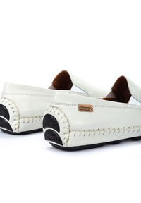 Weiße Leder-Slipper mit runder Zehenpartie, sichtbaren Nähten, Gummisohlen und einem braunen Lederakzentetikett an der Seite.