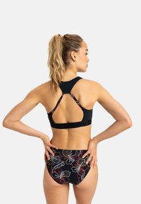 Top de bikini deportivo negro con diseño de espalda corrida y parte inferior con estampado floral en tonos oscuros, que presenta una cinturilla texturizada y herrajes minimalistas.