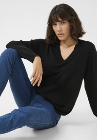 Pull noir à encolure en V avec manches longues, texture douce et coupe décontractée, associé à un jean en denim bleu avec jambes ajustées et détails minimalistes.