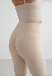 Top corto beige e leggings a vita alta realizzati in un tessuto elastico, con una texture a coste e un logo discreto su entrambi i capi.