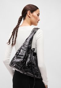 Fekete, fényes, textúrált táska háromszög alakú, hosszú pánttal, amit a vállon viselnek. Fényes, szintetikus anyagból készült.