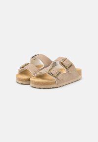 Beige velúr szandálok két állítható pánttal és aranyszínű csatokkal. Parafa talp és gumi talp, melynek mintázata van a tapadás érdekében.