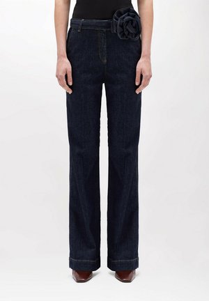 Jeans in denim scuro con design a gamba dritta, caratterizzati da un accento di fiore in tessuto sulla vita. Cuciture a contrasto e tasche standard.