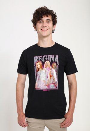 Giovane uomo che indossa una maglietta nera con quattro donne di Mean Girls con la scritta "Regina" sopra e "Mean Girls" sotto.