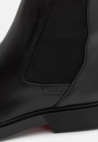 Bottine en cuir noir avec panneaux en mesh texturé, finition lisse, semelle en caoutchouc et marquage discret sur le côté.