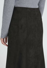 Gonna nera in suede con una texture liscia, caratterizzata da cuciture verticali e una vita semplice. Top grigio a maniche lunghe visibile nella parte superiore.