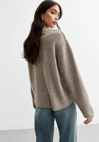 Bruine oversized trui met een ronde halslijn en geribde manchetten, gecombineerd met lichtblauwe denim. Zachte textuur en een ontspannen pasvorm.