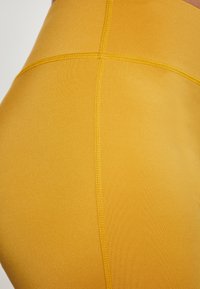 Sárga leggings rugalmas anyagból, sima tapintással, lapos varrással és keresztszámos díszítéssel a derékrészen.
