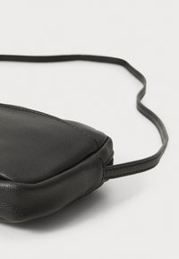 Μαύρη δερμάτινη τσάντα ώμου με λεία υφή, τριγωνικό σχήμα και λεπτό λουρί. Διαθέτει ραφές και μινιμαλιστικό σχέδιο.