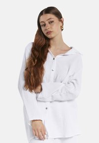 Witte button-up shirt van een gestructureerde, gekreukte stof. Heeft een kraag, lange mouwen en een losse pasvorm met knopen aan de voorkant.