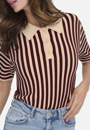 Femme portant un polo beige et bordeaux à rayures verticales manches courtes, rentré dans un jean denim bleu clair.