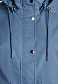 Giacca azzurra realizzata in tessuto liscio, con accessori in argento, chiusura frontale con zip e lacci a corda sul cappuccio e in vita.