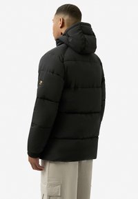 Černá péřová bunda s kapucí, s prošívaným designem, elastickými manžetami a nášivkou s logem na levém rukávu. Hladká textura.