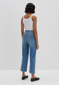 Jeans azzurri chiari a vita alta con gamba dritta, tasche posteriori e una patch di pelle marrone in vita. Abbinati a un top bianco senza maniche.