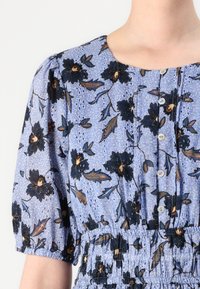 Blå blomstermønstret kjole med korte puffermer, knappestolpe foran, elastisk midje og intrikate blomsterdesign i svart og oransje.