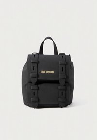 Mochila preta com design estruturado, feita de material resistente. Apresenta uma aba frontal com logotipo dourado e alças ajustáveis com detalhes de fivela.