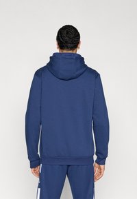 Ναυτικό φούτερ με υφασμάτινη υφή, τσέπη καγκουρό και κουκούλα με κορδόνι. Διαθέτει ριμπ μανσέτες και τελείωμα, συνδυάζεται με αντίστοιχο παντελόνι φόρμας.