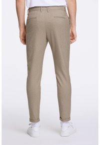 Pantaloni khaki a trama con vestibilità slim, dotati di due tasche posteriori e orli arrotolati, abbinati a sneaker bianche e calze bianche visibili.