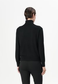 Black turtleneck sweater in fine-knit fabric, featuring long sleeves and ribbed hem. Clean, minimal design with no visible patterns or accents.