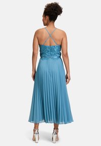 Jasnoniebieska, plisowana sukienka z dopasowaną, haftowaną górą i skrzyżowanymi ramiączkami. Posiada lejącą spódnicę i srebrne szpilki.