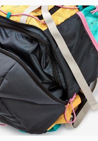 Czarny, teksturowany plecak z żółtymi i turkusowymi akcentami, z siateczkowymi kieszeniami, różnymi zamkami błyskawicznymi i kolorowymi paskami.