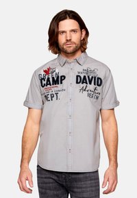 Camisa de botones de manga corta gris con texto bordado y un diseño de hoja de arce. Tejido suave con un ajuste relajado.