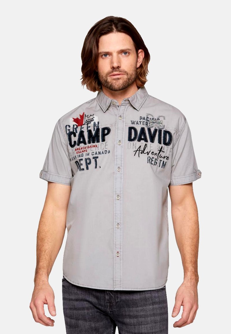 Camisa de botones de manga corta gris con texto bordado y un diseño de hoja de arce. Tejido suave con un ajuste relajado.