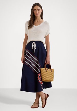 Femme portant un haut en maille blanc à manches courtes et une jupe midi bleu marine à rayures diagonales, tenant un sac tissé et portant des sandales.