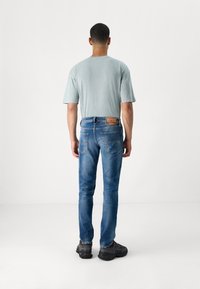 Vaaleansininen puuvillainen lyhythihainen t-paita, yhdistetty tummansinisiin farkkuihin ja mustiin lenkkareihin, nähtynä takaa.