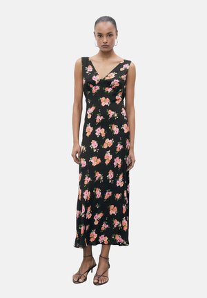 Abito nero floreale con fiori rosa e arancio, scollo a V, senza maniche, tessuto leggero, lunghezza al ginocchio, indossato con sandali con cinturini.