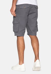 Graue Cargo-Shorts aus Baumwolle, ausgestattet mit mehreren Seitentaschen und einem geraden Schnitt, kombiniert mit weißen Sneakers.