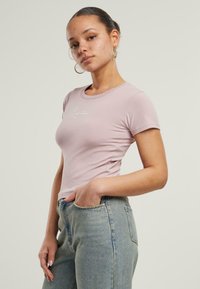 Lys rosa tettsittende T-skjorte med korte ermer, med en subtil brodert design. Kombinert med høyt liv blå denimjeans.