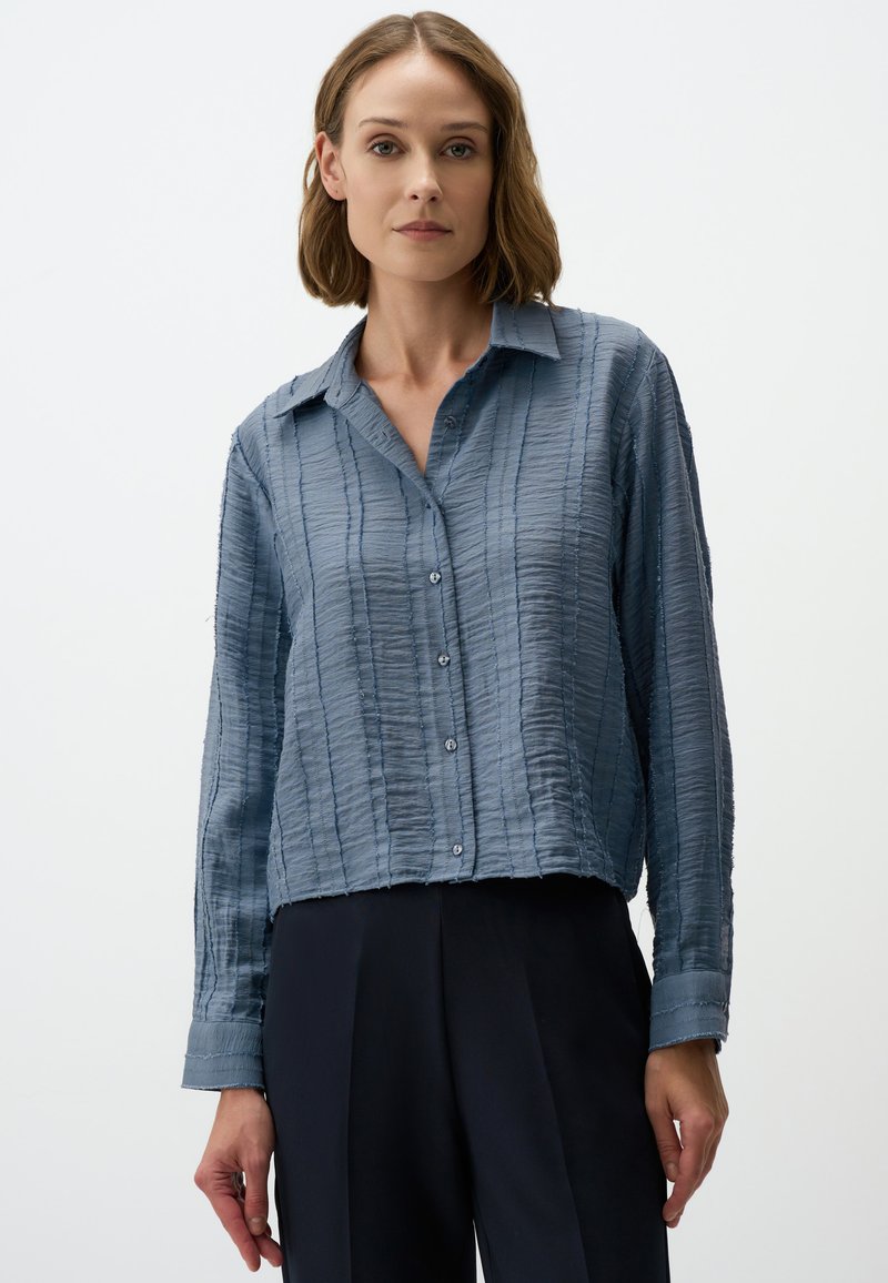 Lichtblauwe gestructureerde blouse met een cropped snit, knoopsluiting aan de voorkant en lange mouwen. Heeft een zachte, gekreukte stof en een kraag.