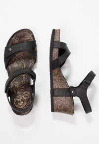 Des sandales compensées noires avec des sangles ajustables et un design floral sur la semelle intérieure, présentées en vue de dessus et de côté sur un fond blanc.