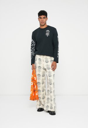Camicetta nera a maniche lunghe con design floreale, abbinata a pantaloni larghi color crema con un motivo a foglie grigie. Borsa arancione con fiori bianchi.