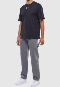 Camiseta de algodón negra con un logo blanco en el pecho, combinada con jeans rectos gris y zapatillas blancas.