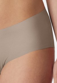 Beige hipster briefs made of smooth fabric, featuring a seamless design with a mid-rise waistband. Soft texture and matte finish.