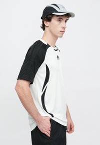 Biała sportowa koszulka z czarnymi akcentami i paskami, krótkimi rękawami i lekkim materiałem. Do kompletu czapka w kolorze czarno-szarym.